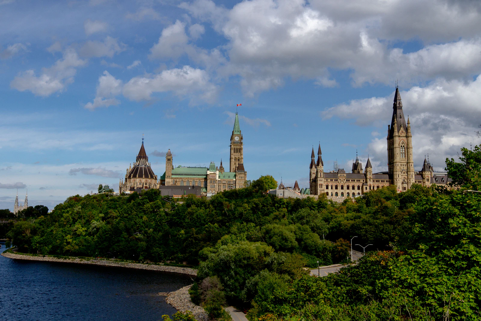 A historic stone government building framed by green trees under a clear blue sky in Ottawa Ontario