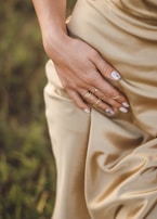 Close-up of a model’s hand adorned with delicate rings, holding a mauve clutch on a cobblestone street.