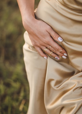 Soft-focus shot of a hand adorned with gold rings gently touching a charcoal gray silk fabric.