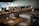 Tables set with wine glasses and cloth napkins inside a dimly lit, modern restaurant featuring wooden furniture and soft lighting.