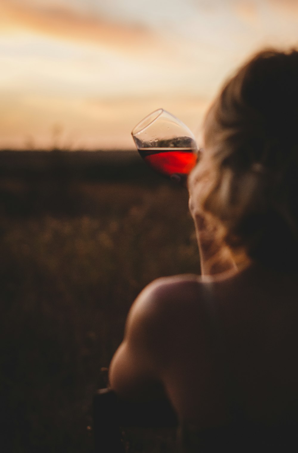 a woman sitting in a field with a glass of wine in her hand