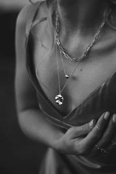 Elegant lifestyle image of a woman gently touching her neck, showcasing layered jewelry.