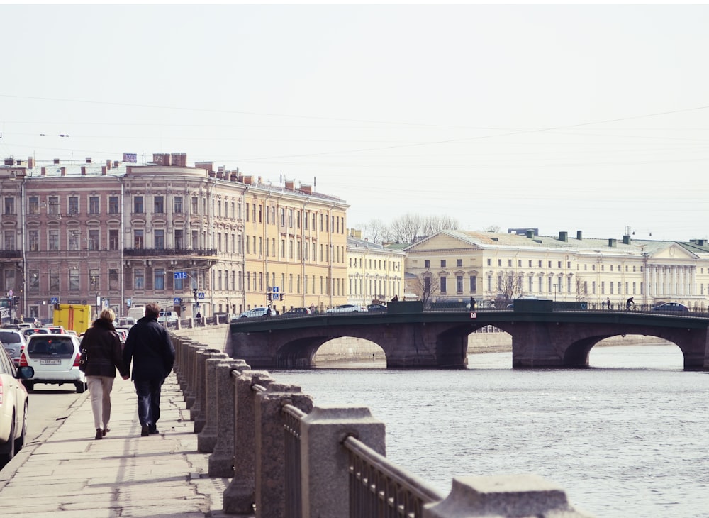 man in black jacket walking on sidewalk near river during daytime