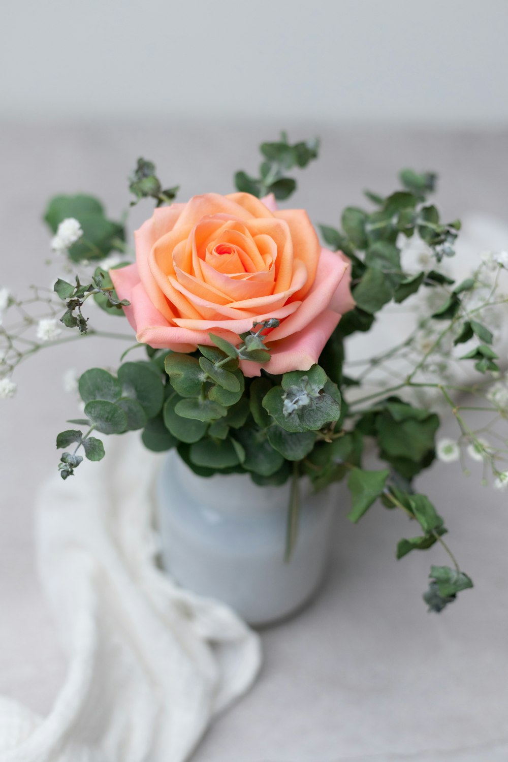 a small vase with a pink rose and greenery