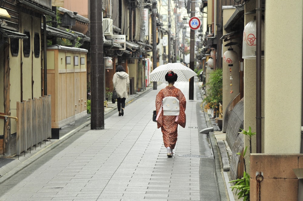 femme en kimono rouge tenant un parapluie marchant sur le trottoir pendant la journée