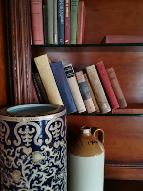Close-up of a modern ceramic vase in soft brown resting on a light wooden shelf among books.