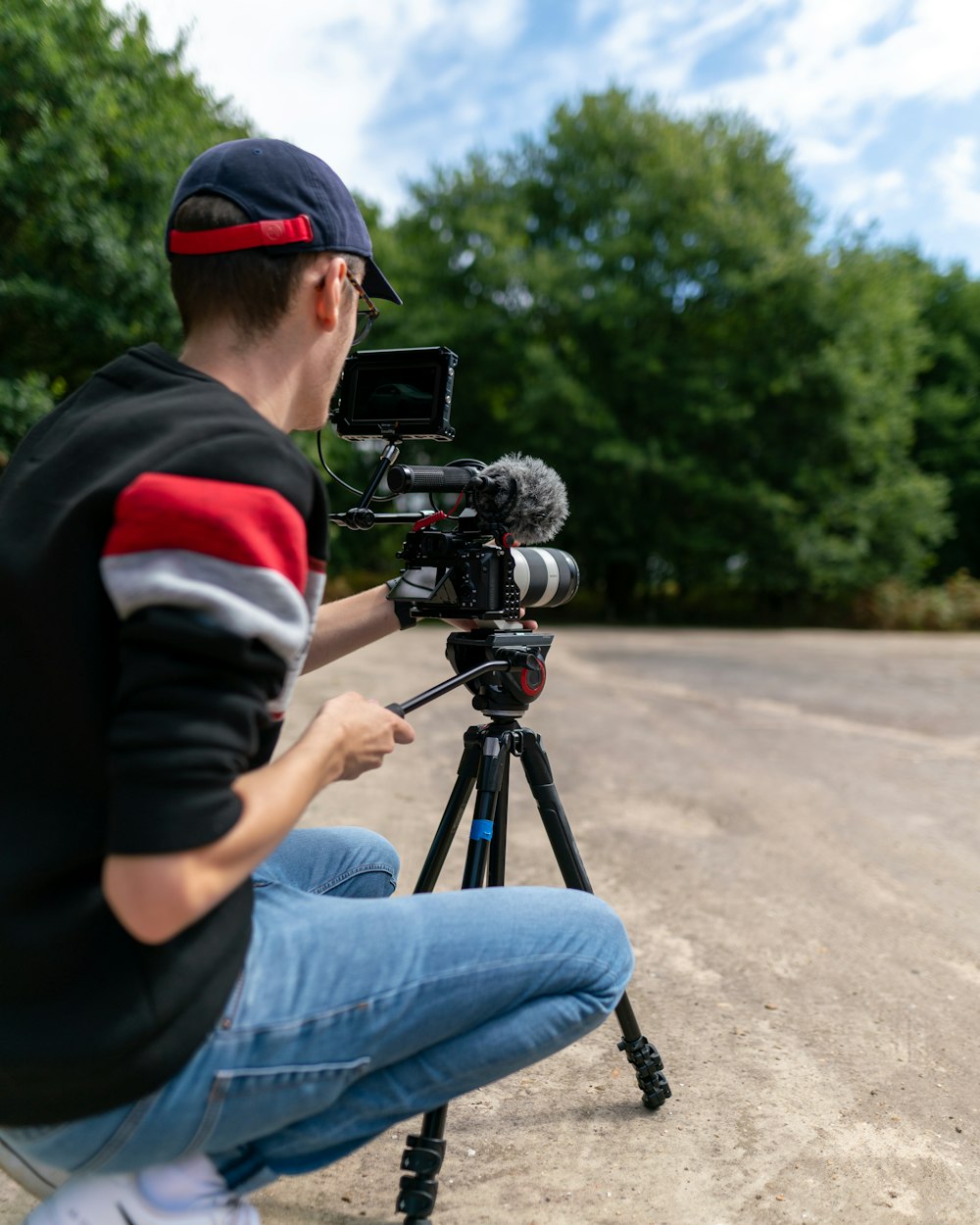 man in black and red jacket and blue denim jeans holding black video camera