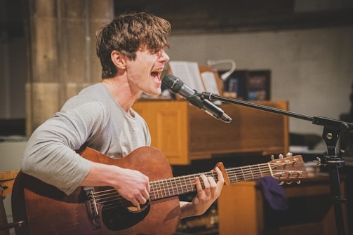man in gray v neck long sleeve shirt playing brown acoustic guitar