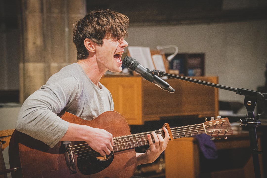 man in gray v neck long sleeve shirt playing brown acoustic guitar