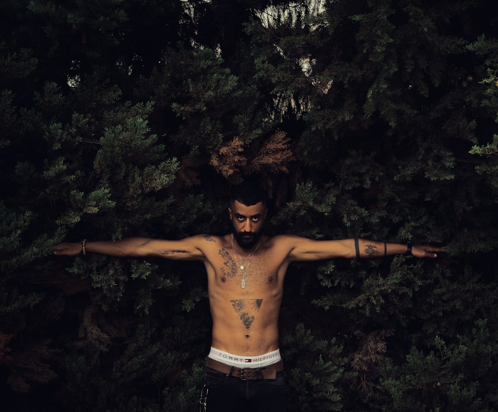 topless man in black shorts standing near green trees during daytime