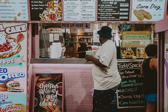 man in white long sleeve shirt and black pants standing in front of food stall