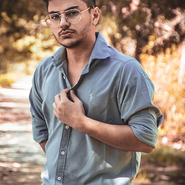 A man in a light blue button-down shirt and glasses in a sunlit park
