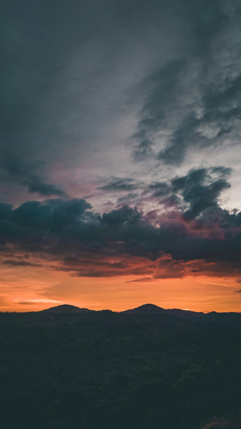 silhouette of mountains under cloudy sky during sunset