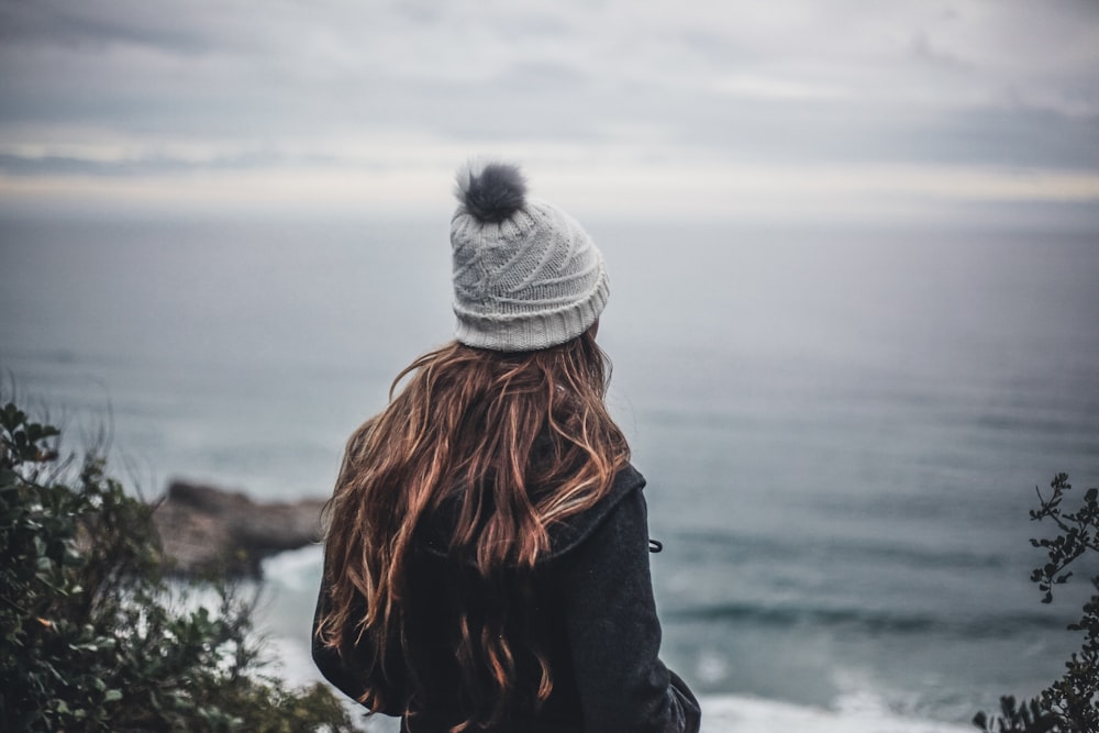 woman in black jacket and gray knit cap standing near body of water during daytime