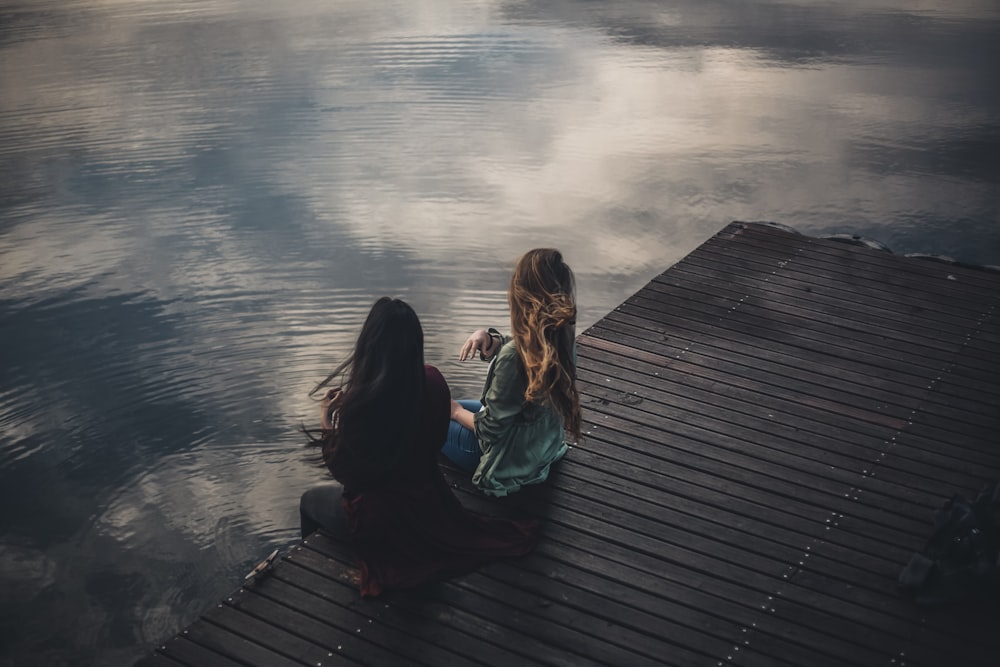 2 women sitting on wooden dock during daytime