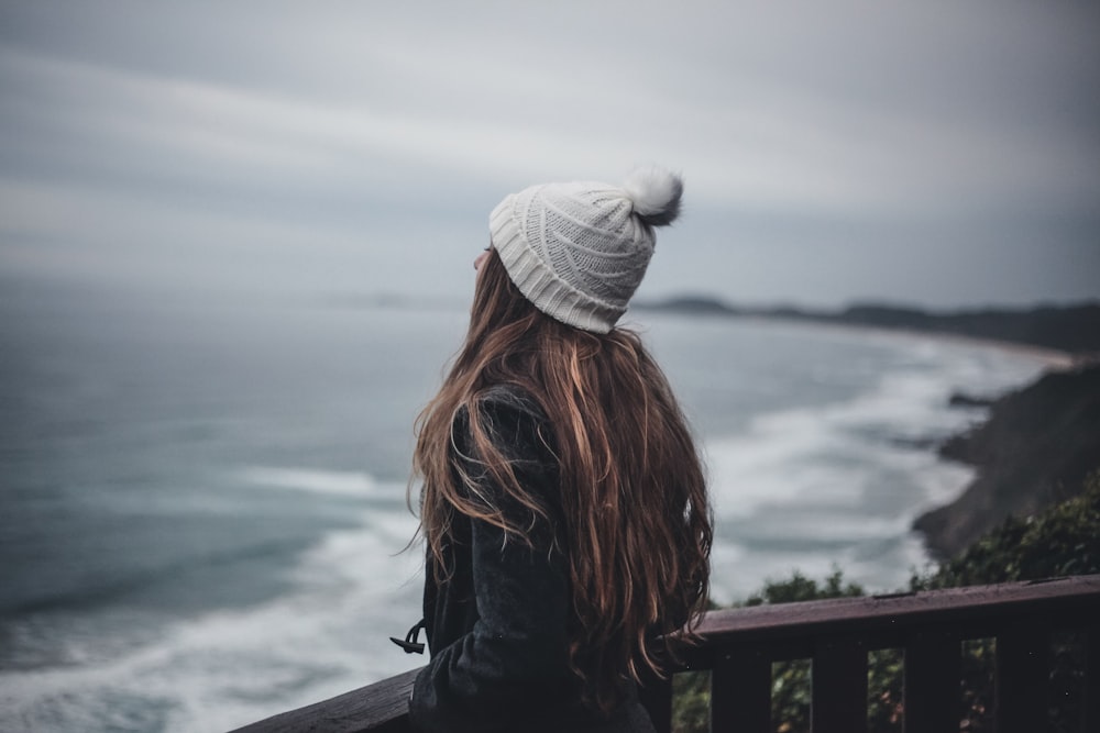 woman in black jacket and gray knit cap standing near body of water during daytime