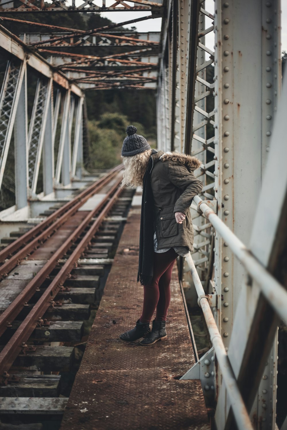 woman in brown jacket walking on brown wooden bridge during daytime