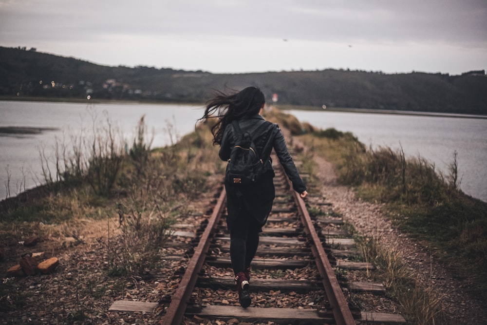 woman in black jacket walking on brown wooden bridge during daytime