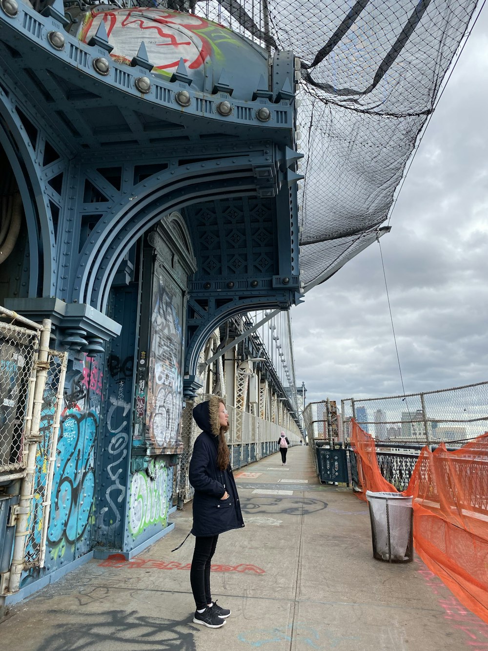 woman in black jacket walking on bridge during daytime