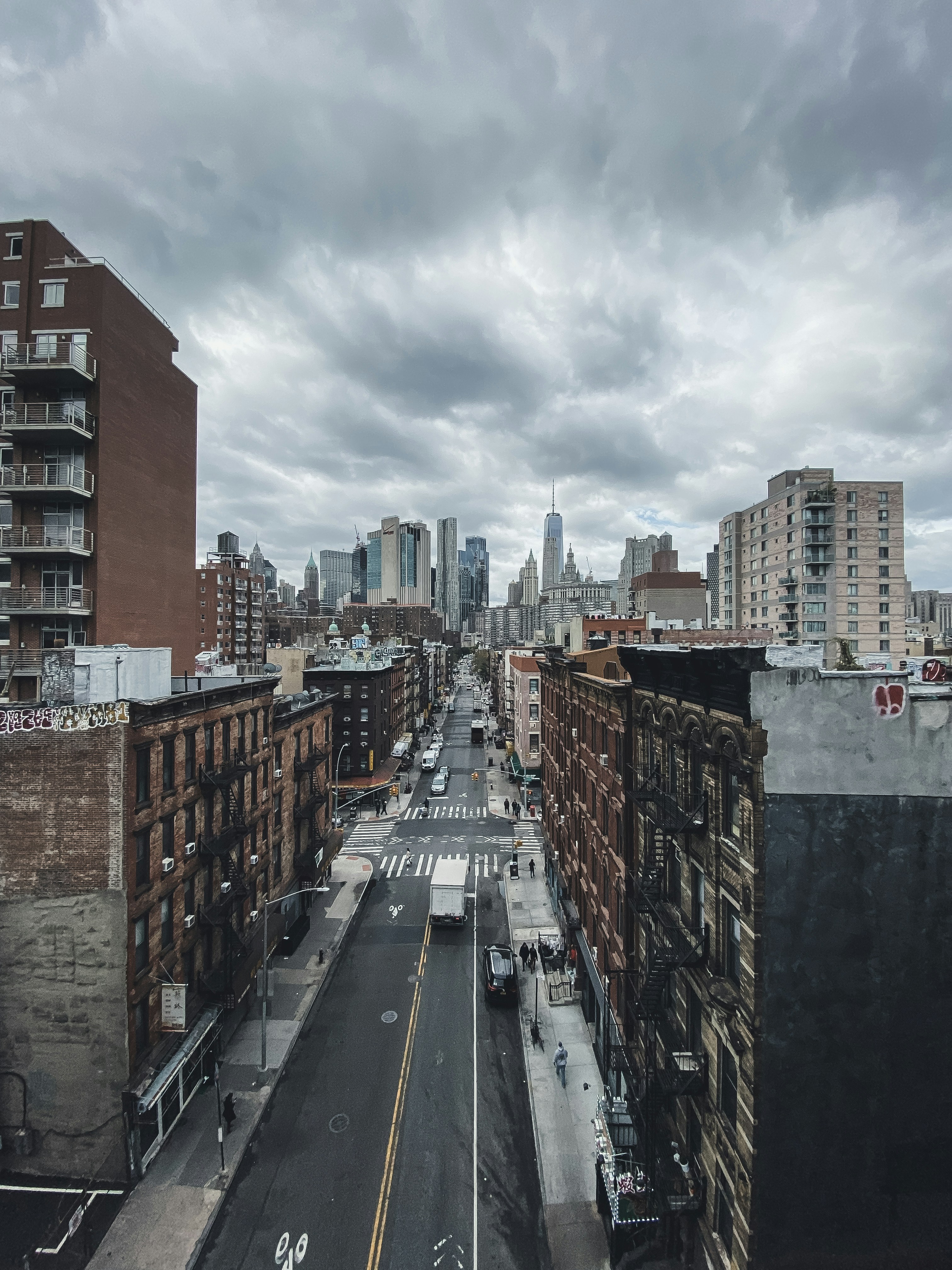 cars on road between high rise buildings under white clouds and blue sky during daytime