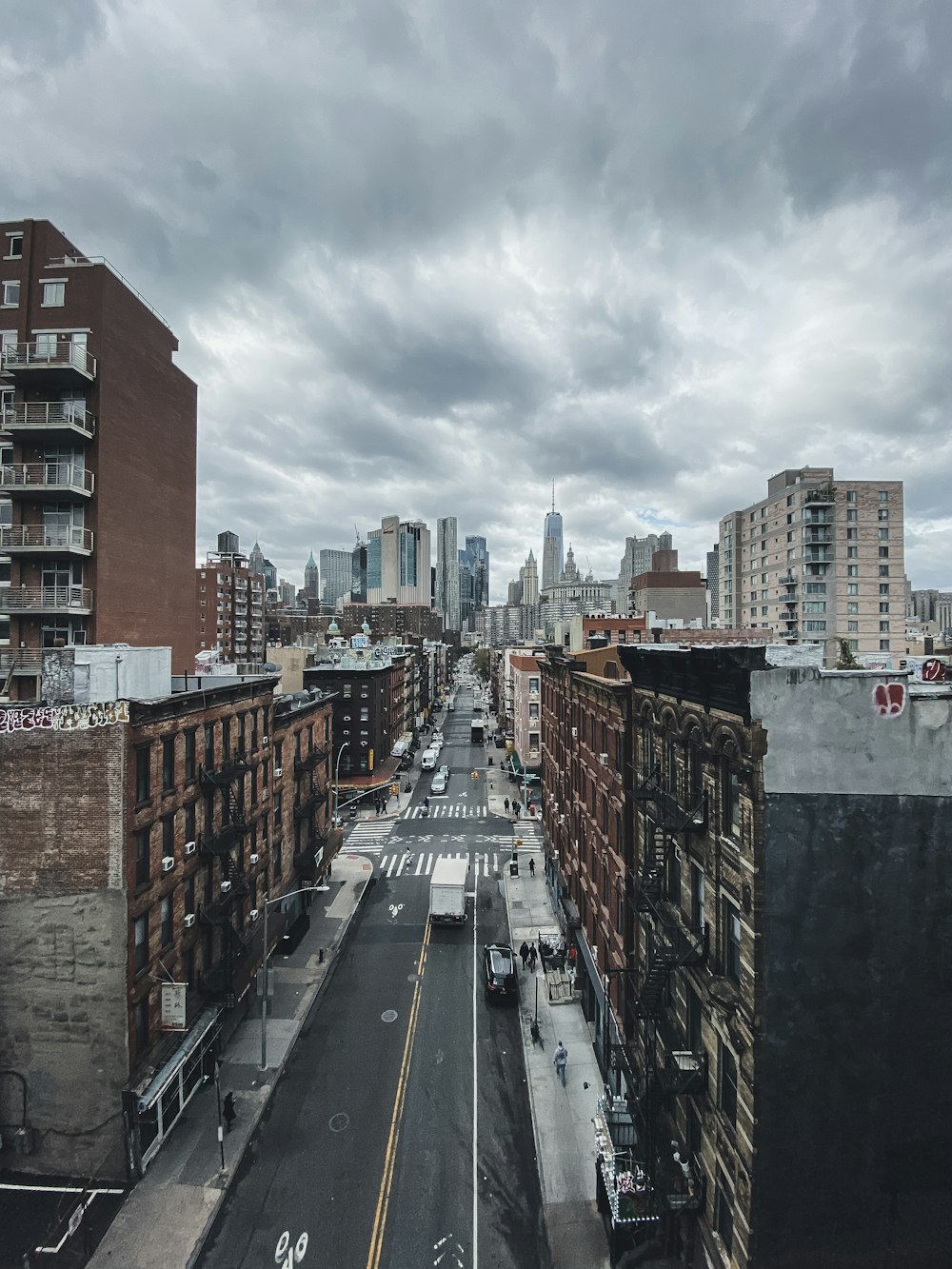 cars on road between high rise buildings under white clouds and blue sky during daytime