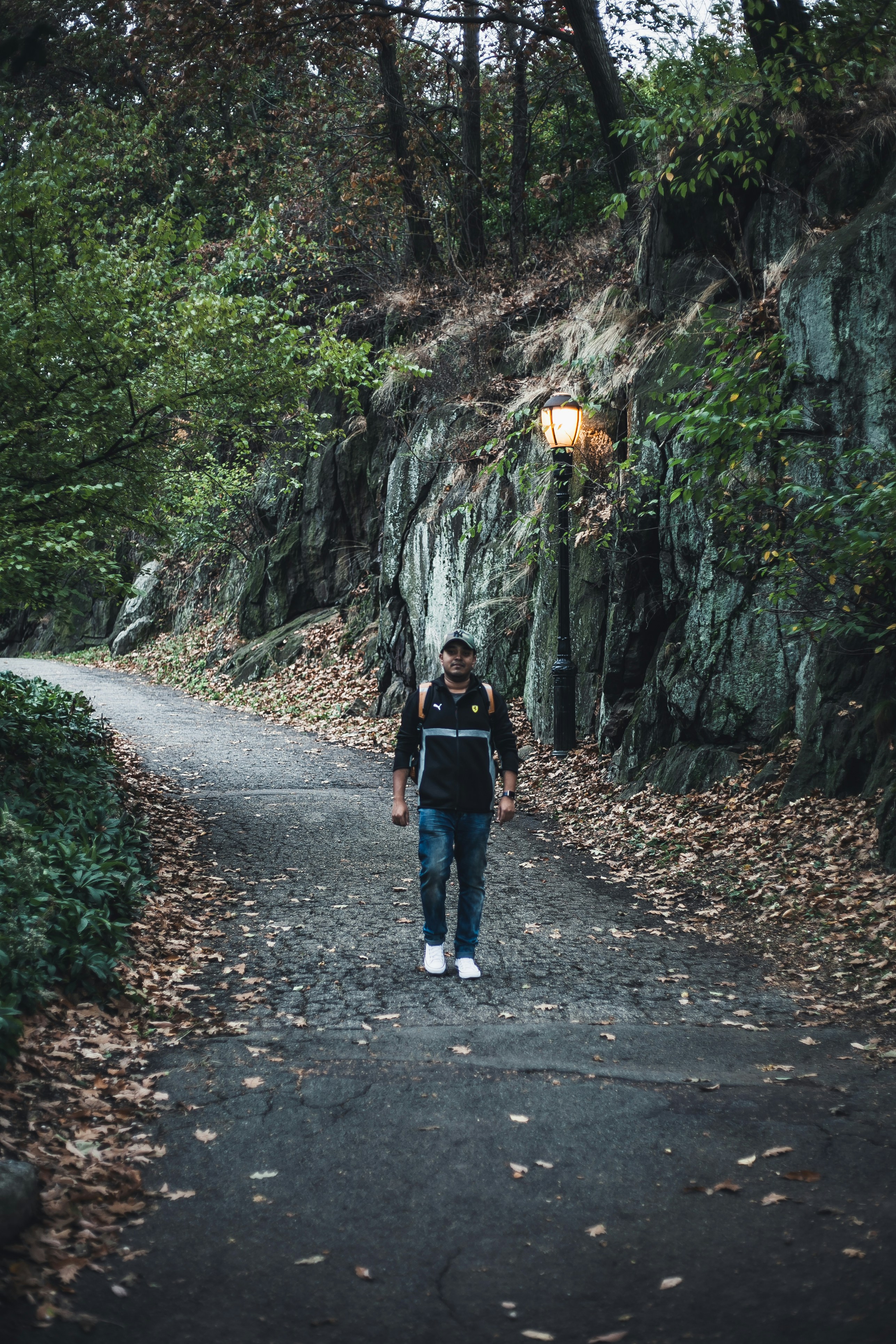 woman in black jacket and blue denim jeans walking on pathway between rocky mountains during daytime