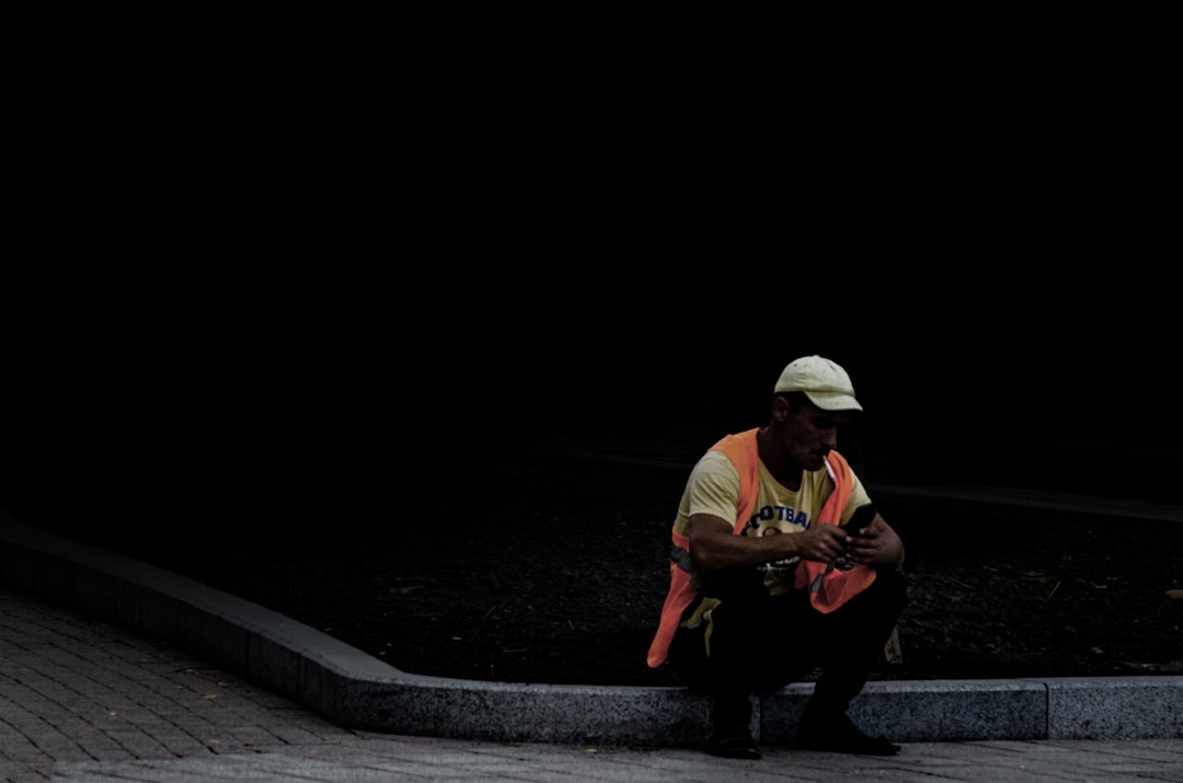 man in white shirt playing guitar sitting on concrete pavement