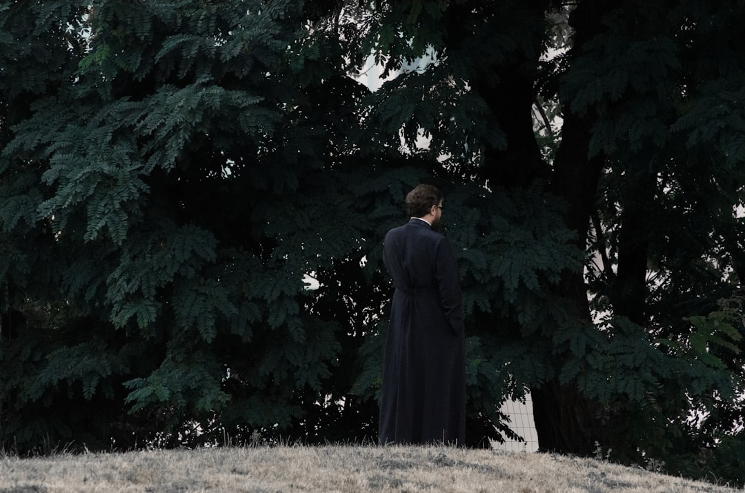 man in black suit standing near green tree during daytime