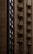A tall building with a facade made of brown bricks. The structure features multiple small balconies, each equipped with an air conditioning unit. The windows are modern and vertically aligned, contributing to a streamlined architectural appearance.