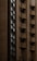 A tall building with a facade made of brown bricks. The structure features multiple small balconies, each equipped with an air conditioning unit. The windows are modern and vertically aligned, contributing to a streamlined architectural appearance.