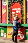 A person is standing at a fast-food stand, dressed in a blue sports jersey with the number 10 and the word 'France' on the back. The surrounding display has vibrant advertisements featuring various food items like french fries, coffee, hot dogs, and other snacks, alongside prices in Ukrainian currency. The backdrop includes bold and colorful signage, creating a lively and busy atmosphere.