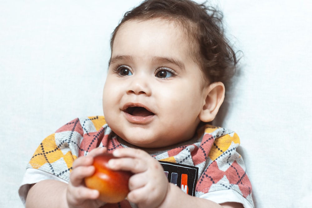 child in white red and blue shirt holding red tomato