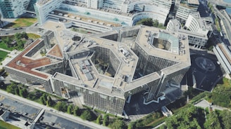Aerial view of a large, modern architectural structure surrounded by greenery and urban landscape.