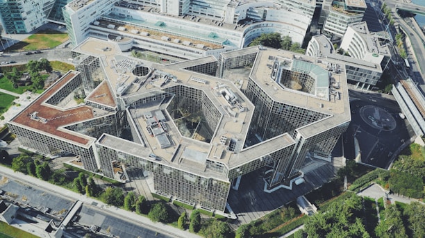 Aerial view of a large, modern architectural structure surrounded by greenery and urban landscape.