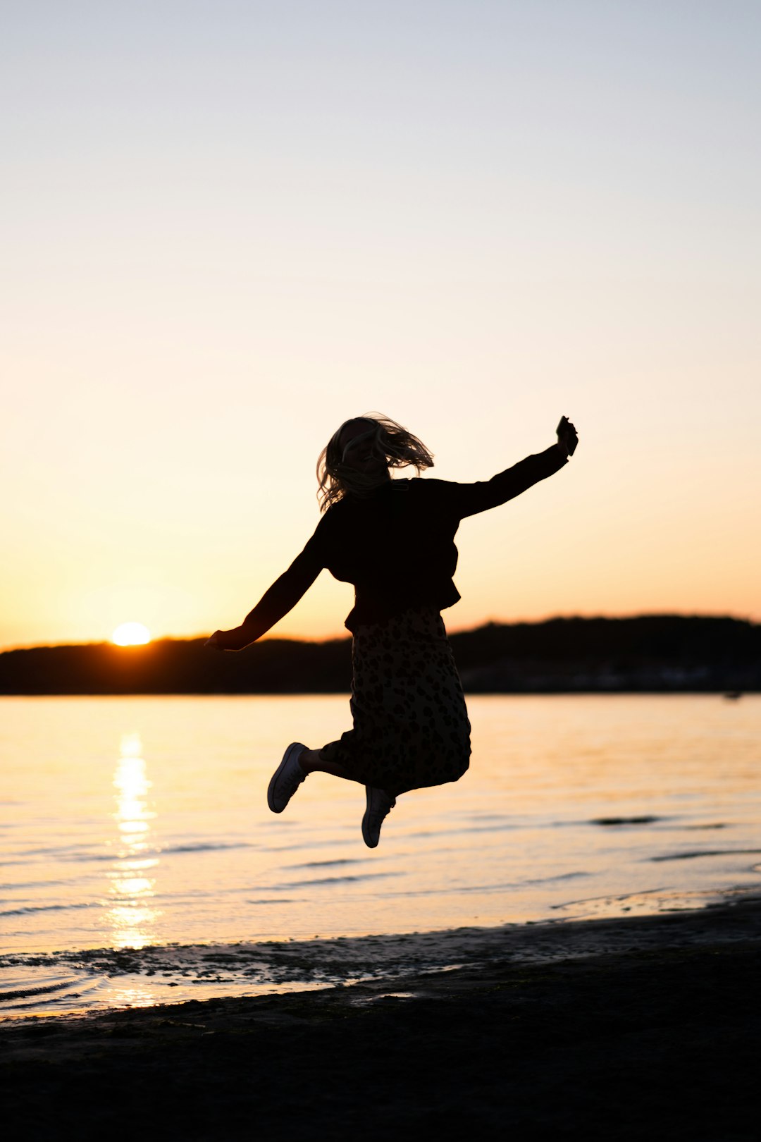 girl in black dress jumping on water during sunset