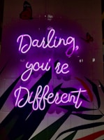 Neon pink cursive text reads 'Darling, you're different' against a dark background. Two butterflies are visible, one at the top left and another at the top right. The background features abstract shapes in shades of red, green, and black.