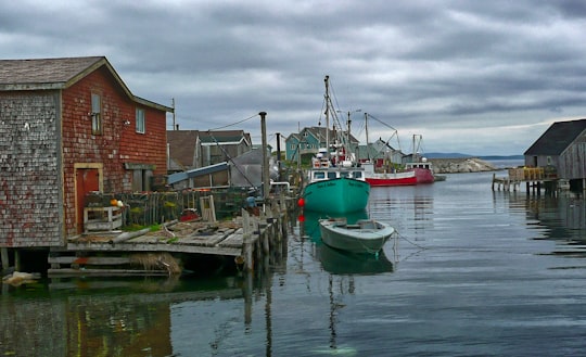 green and white boat on water near brown concrete building during daytime in Peggy's Cove Canada