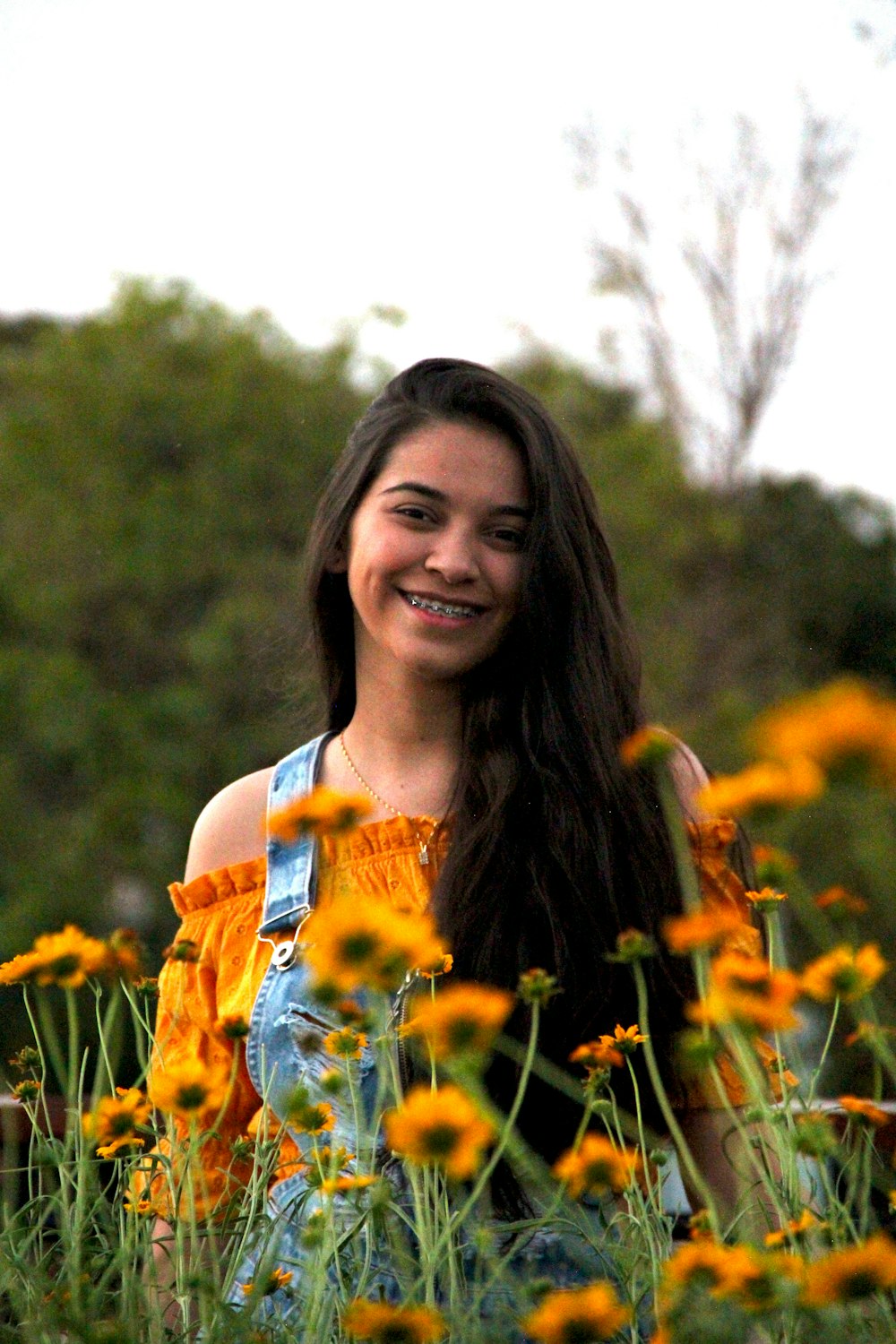 Mujer en camiseta sin mangas floral azul y blanca de pie en el campo de flores amarillas durante el día