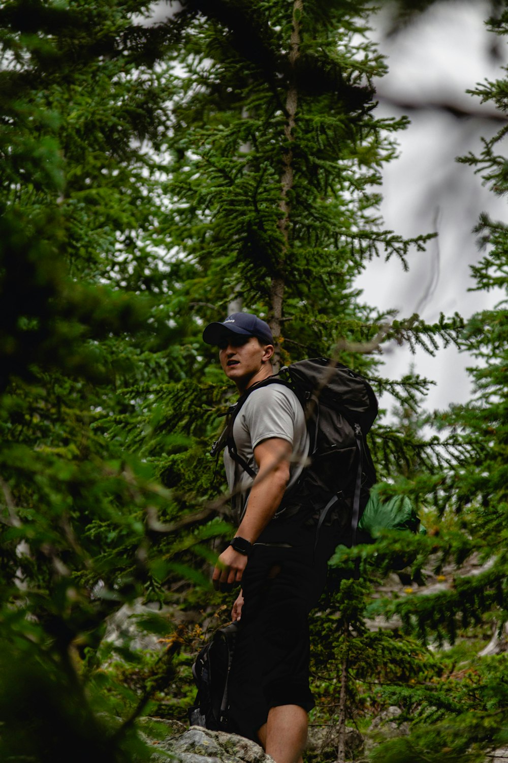 man in grey t-shirt and black pants with black backpack standing near green trees during