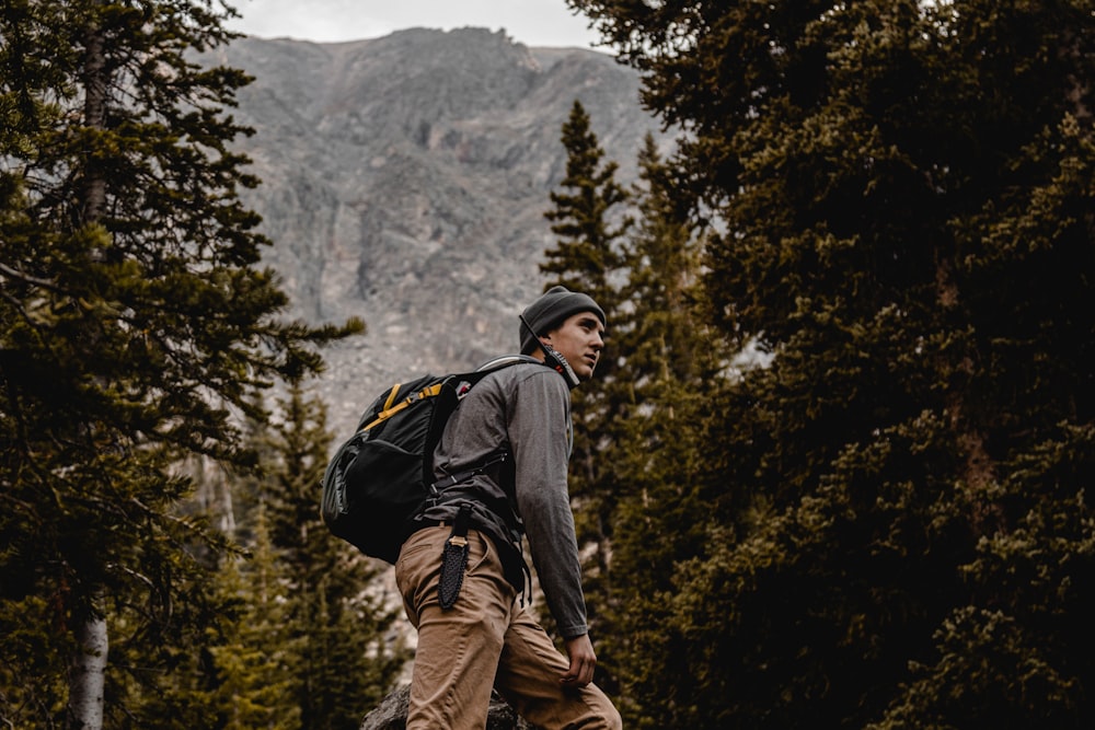 man in black jacket and brown pants with backpack standing on rock looking at snow covered