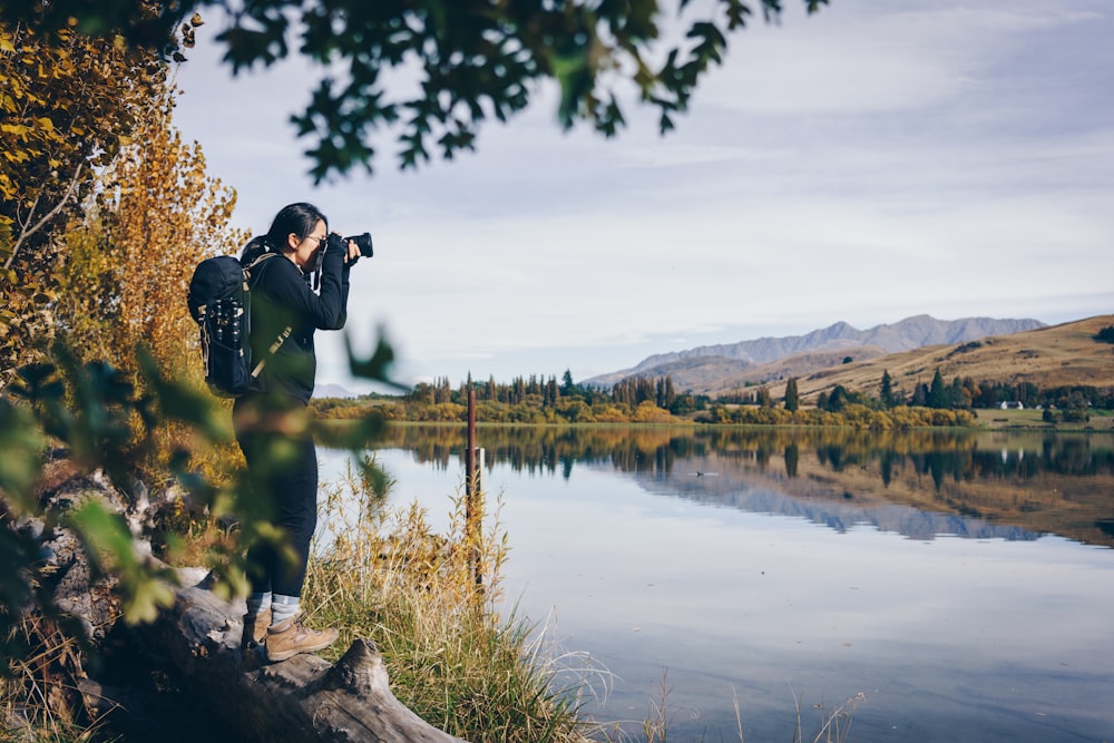 uomo in giacca nera che scatta foto del lago durante il giorno