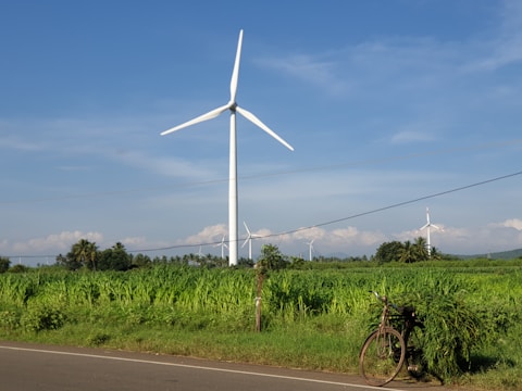 white wind turbine on green grass field under blue sky during daytime