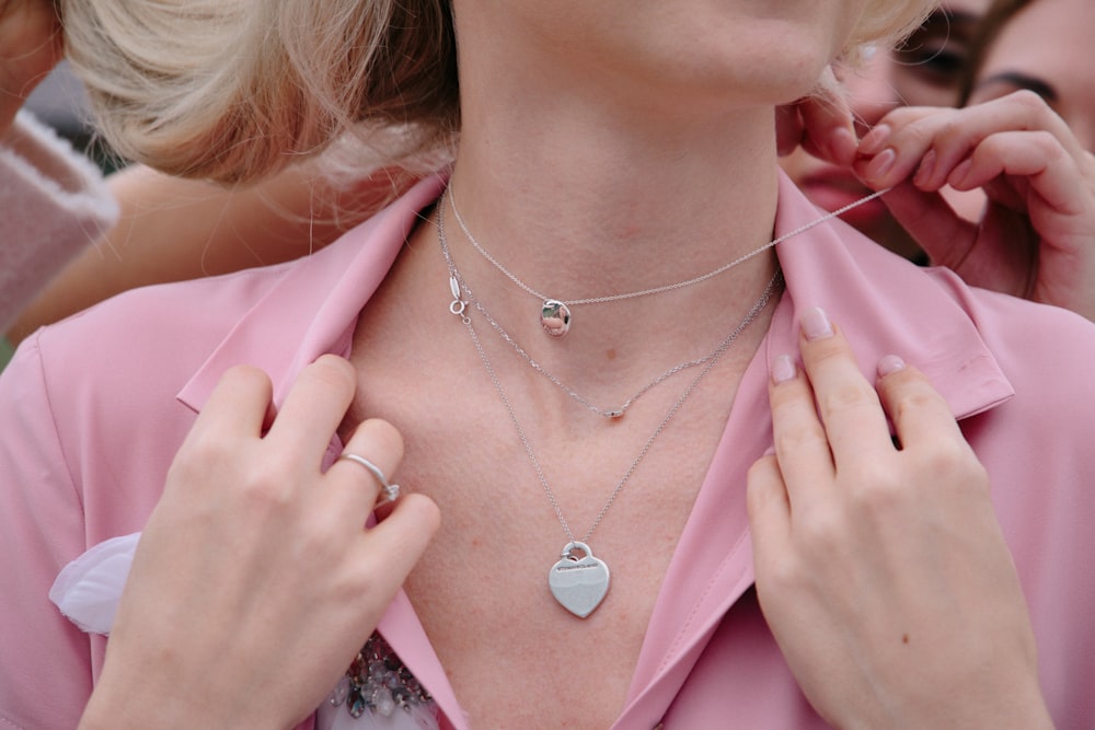 Femme en blazer rose portant un collier pendentif coeur en argent