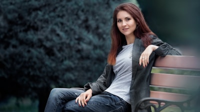 woman in gray long sleeve shirt and blue denim jeans sitting on green wooden bench