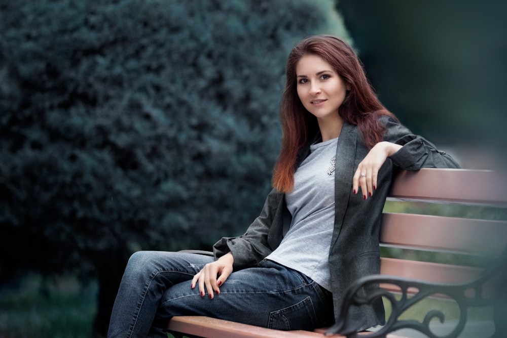 woman in gray long sleeve shirt and blue denim jeans sitting on green wooden bench