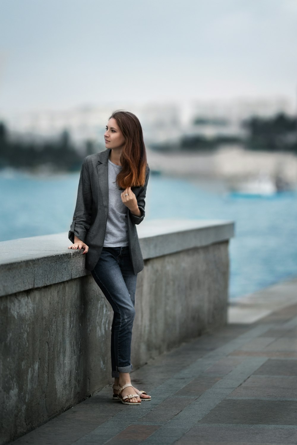 woman in gray blazer and blue denim jeans standing on gray concrete wall during daytime