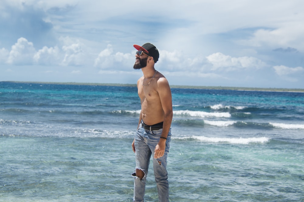 topless man in blue denim jeans standing on beach during daytime