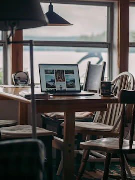 A cozy wooden table with old family photographs and a laptop displaying the mossnest portal.