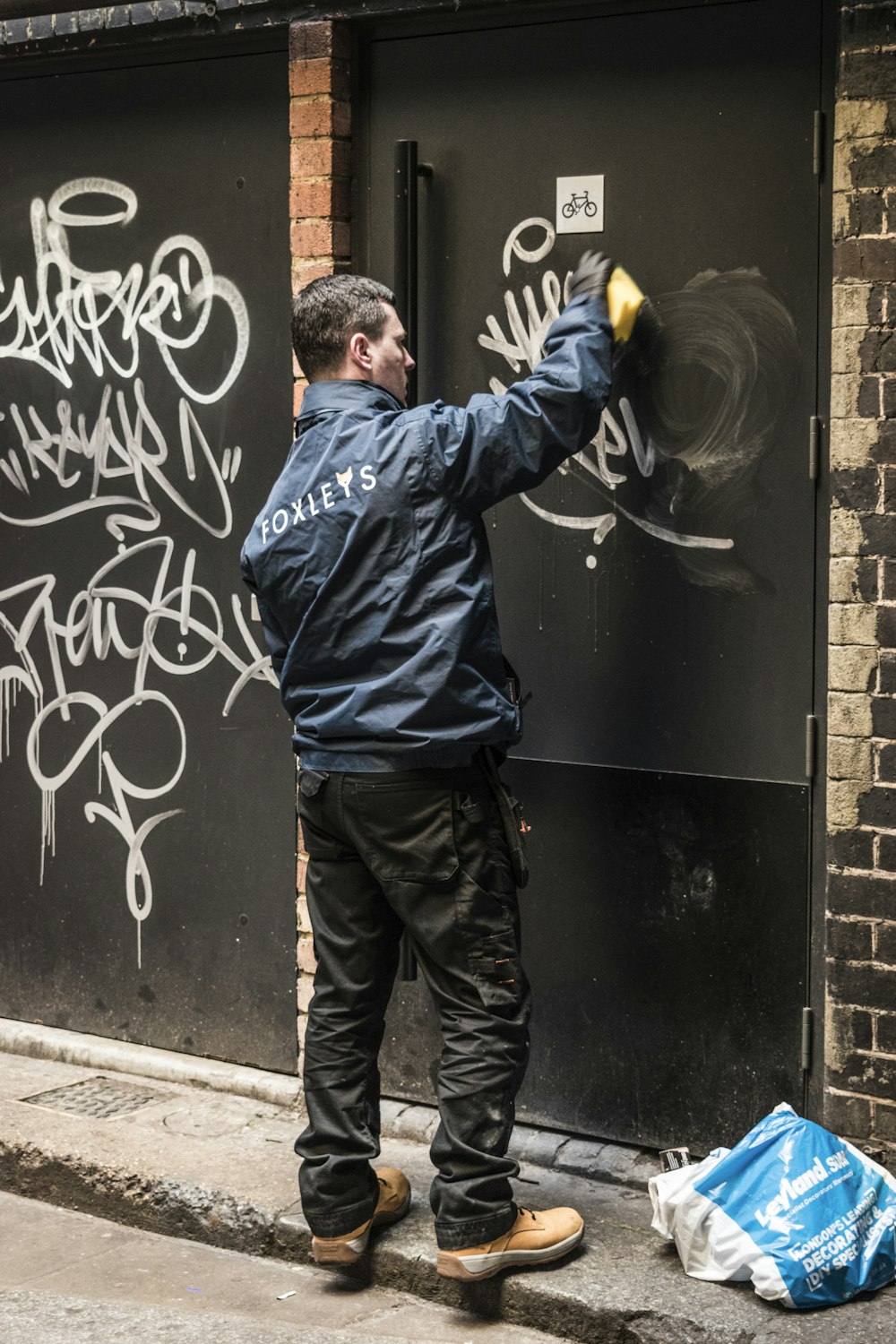 Hombre con chaqueta azul y jeans de mezclilla azules de pie junto a la puerta de madera negra