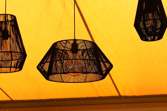 Three hanging pendant lights with a woven design against a vibrant yellow background.